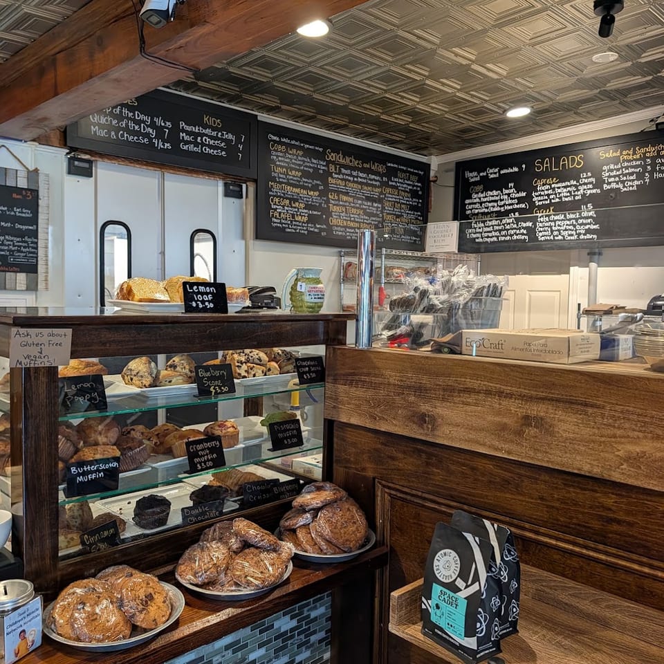 A bakery interior with a display case full of muffins and scones, and menu boards above.