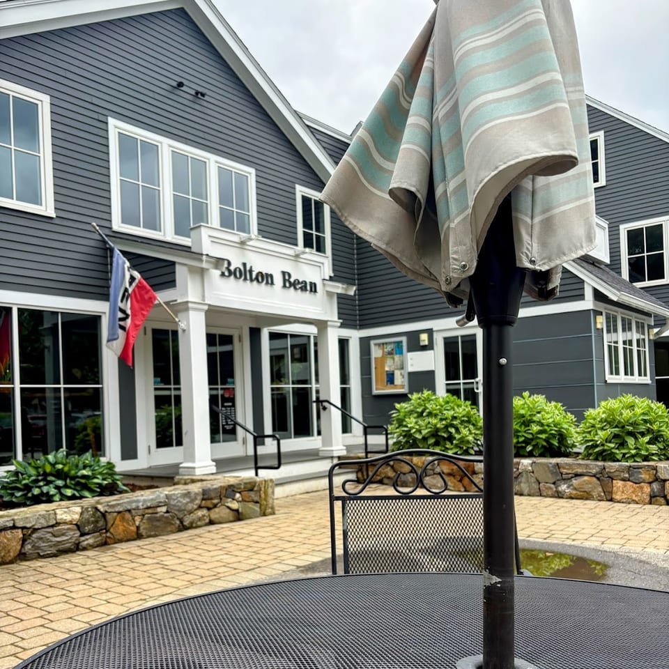 Outdoor patio table with umbrella, overlooking the Bolton Bean coffee shop entrance on a cloudy day.